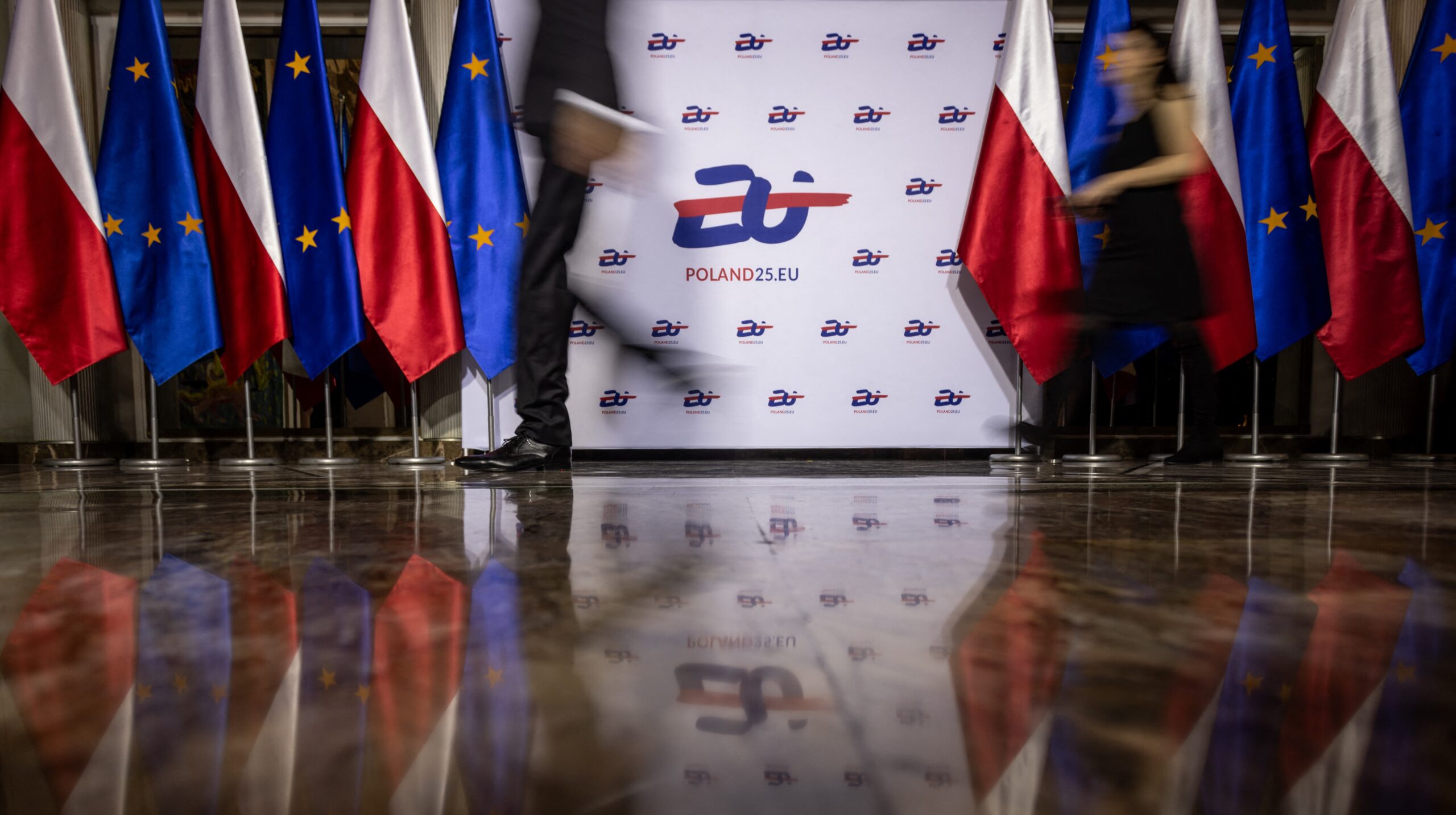 People pass by the logo of the Polish Presidency, at the Polish National Opera in Warsaw on 3 January 2025, before a gala to mark the official opening of the Polish presidency of the Council of the European Union